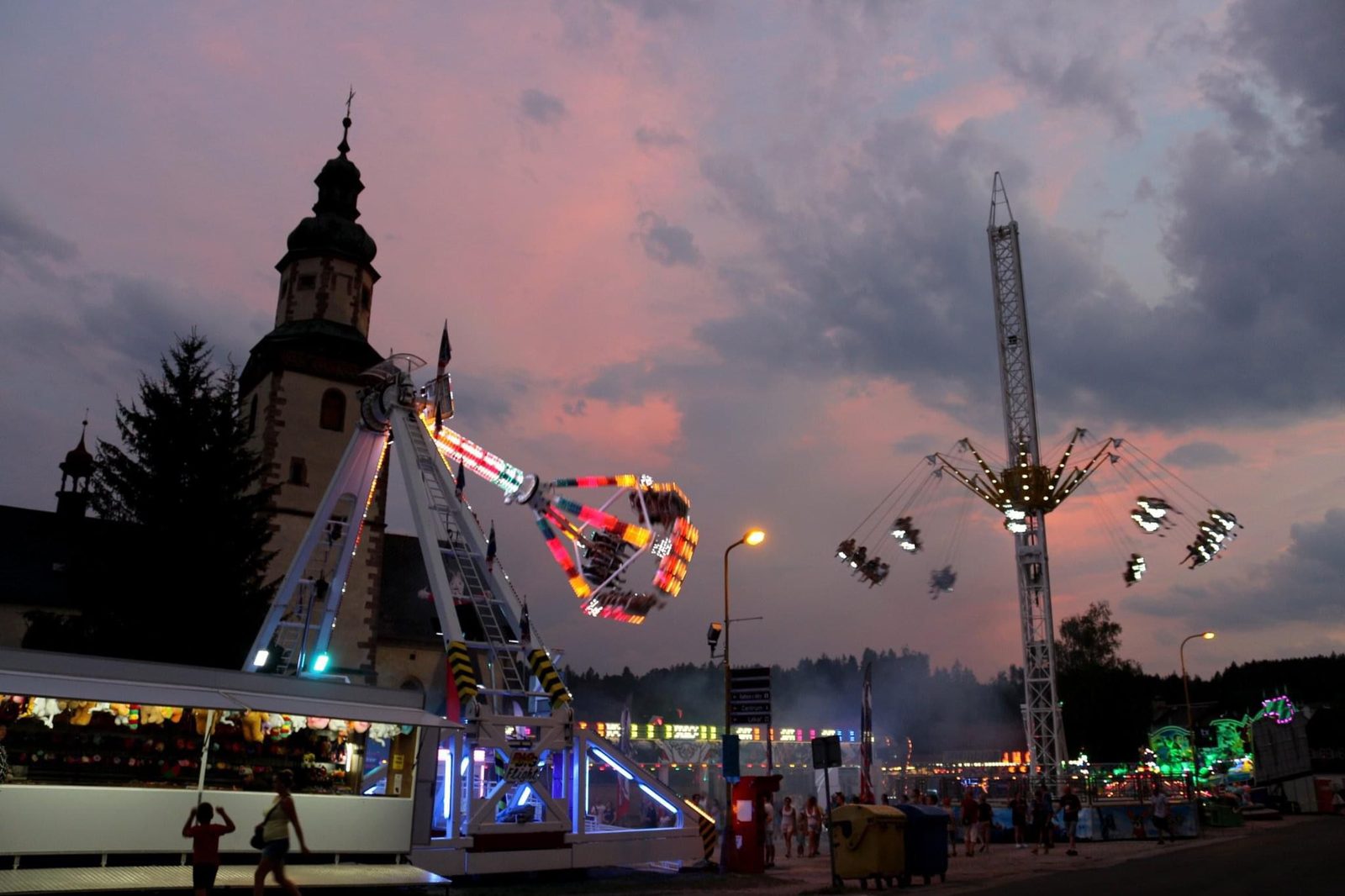 Řetízkový kolotoč a věž kostela za soumraku